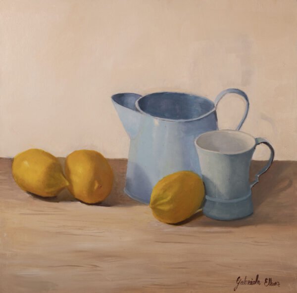 A blue pitcher and cup beside three lemons on a wooden surface.