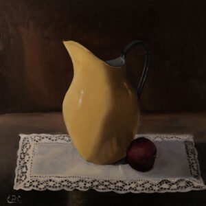 A yellow ceramic pitcher next to a red onion on a lace tablecloth.