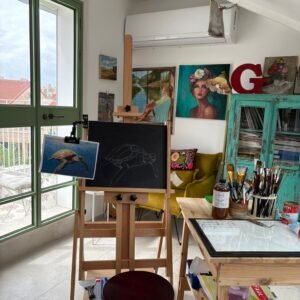 An art studio featuring an easel, paint supplies, and artwork on the walls.